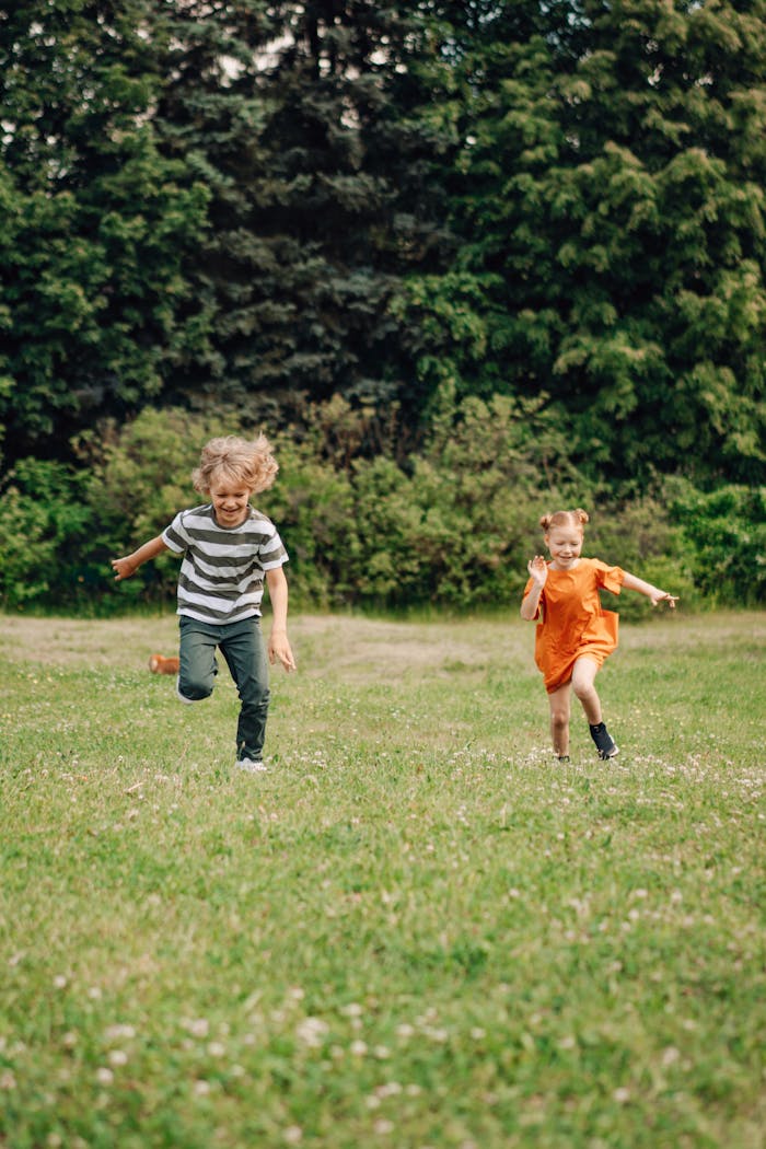 Two happy children joyfully running on a sunny day in a lush green field, enjoying outdoor fun.
